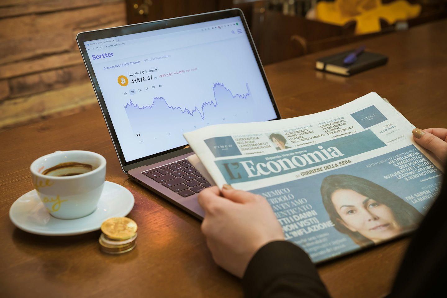 Mani che tengono un giornale finanziario vicino a un laptop con grafici Bitcoin.
