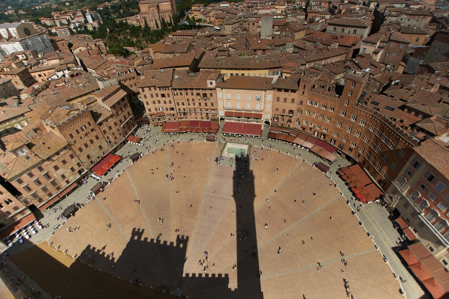 Persone attraversano la grande piazza cittadina pavimentata a forma di ventaglio.
